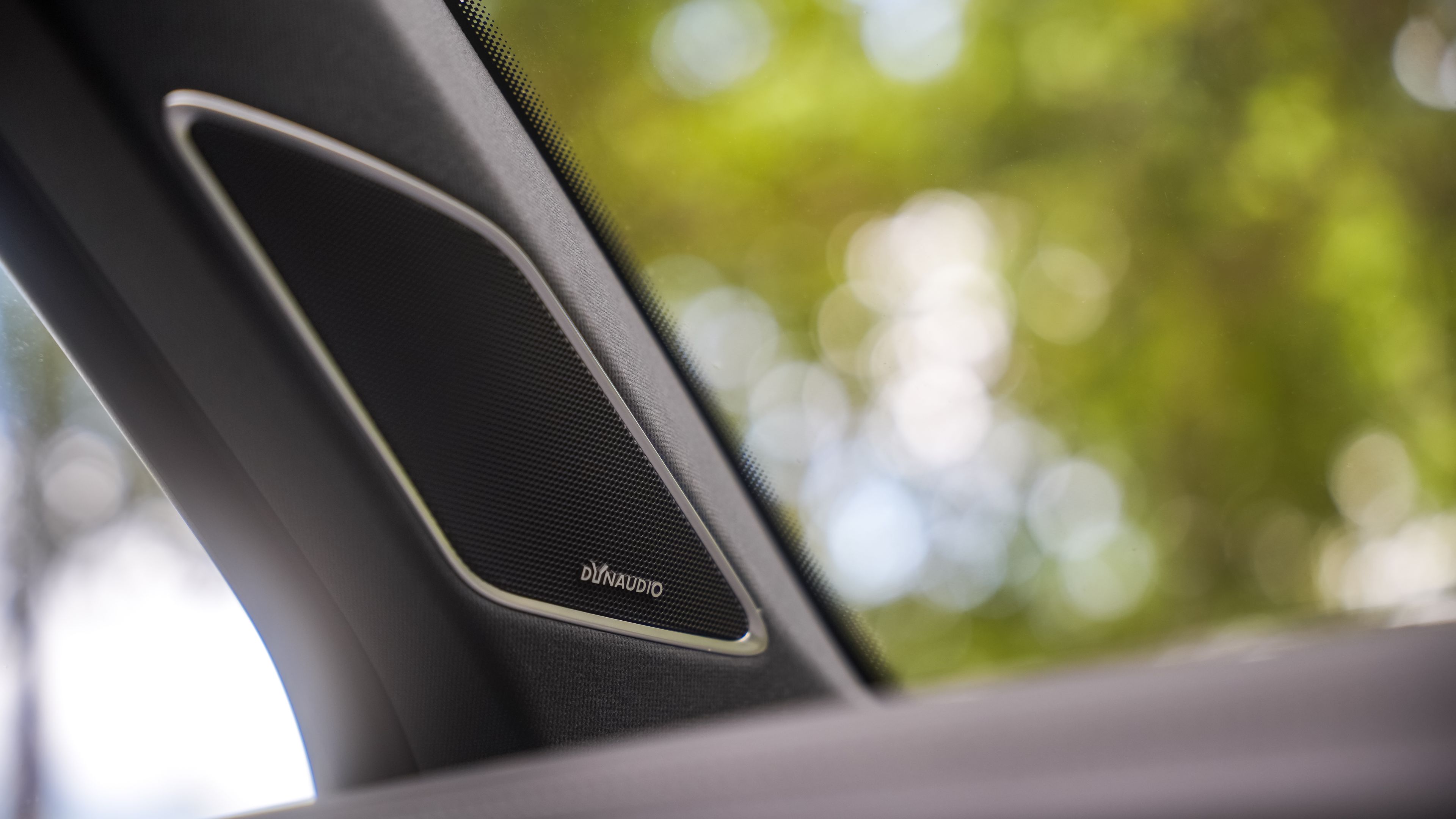 Volkswagen Touareg R-Line | 730-watt Dynaudio Consequence sound system Vehicle door panel of a Volkswagen Touareg R-Line with a Dynaudio sound system speaker, blurred trees visible through the window.