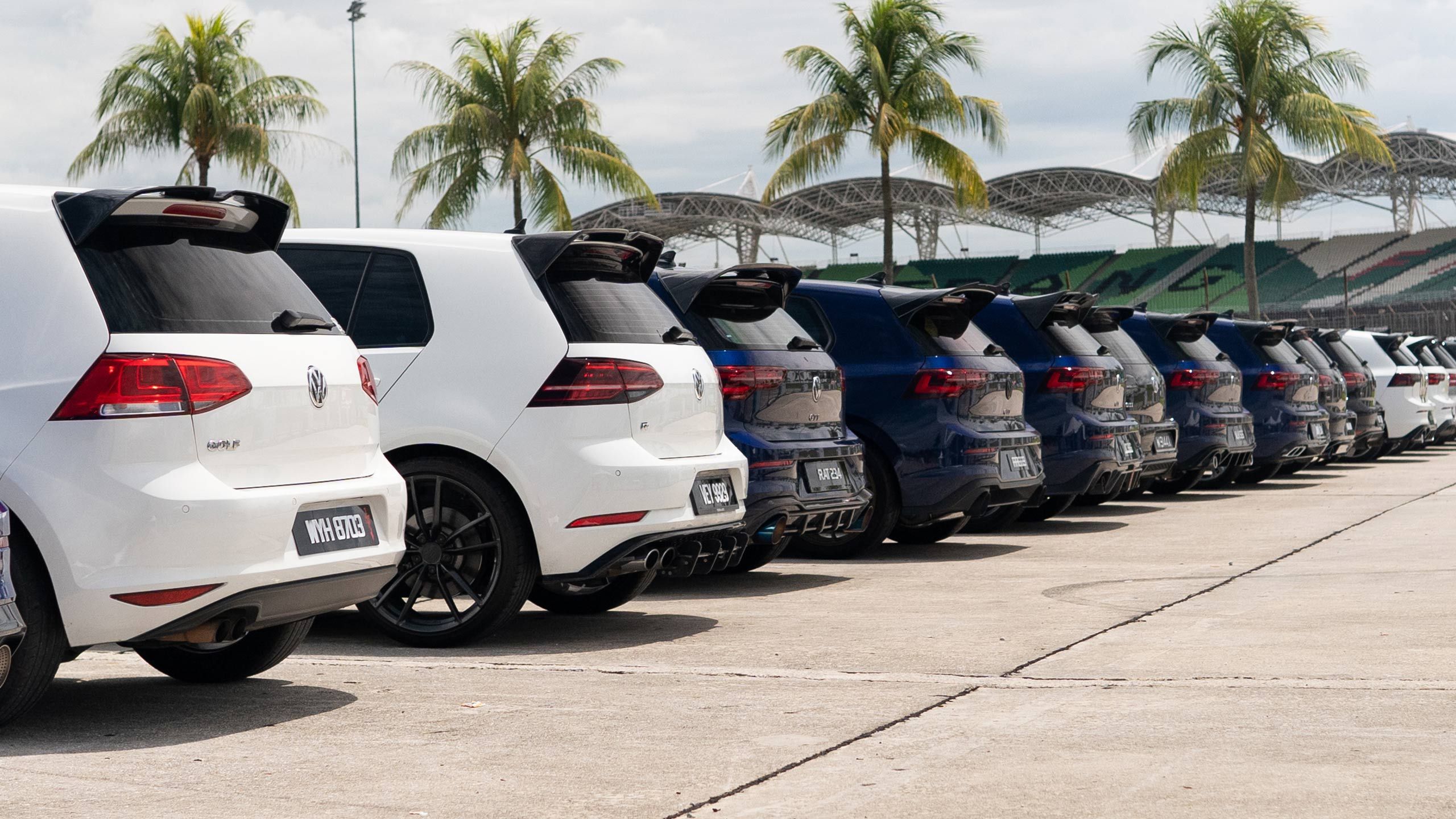 Golf Showdown A row of Volkswagen cars, mostly hatchbacks, parked in an outdoor lot.