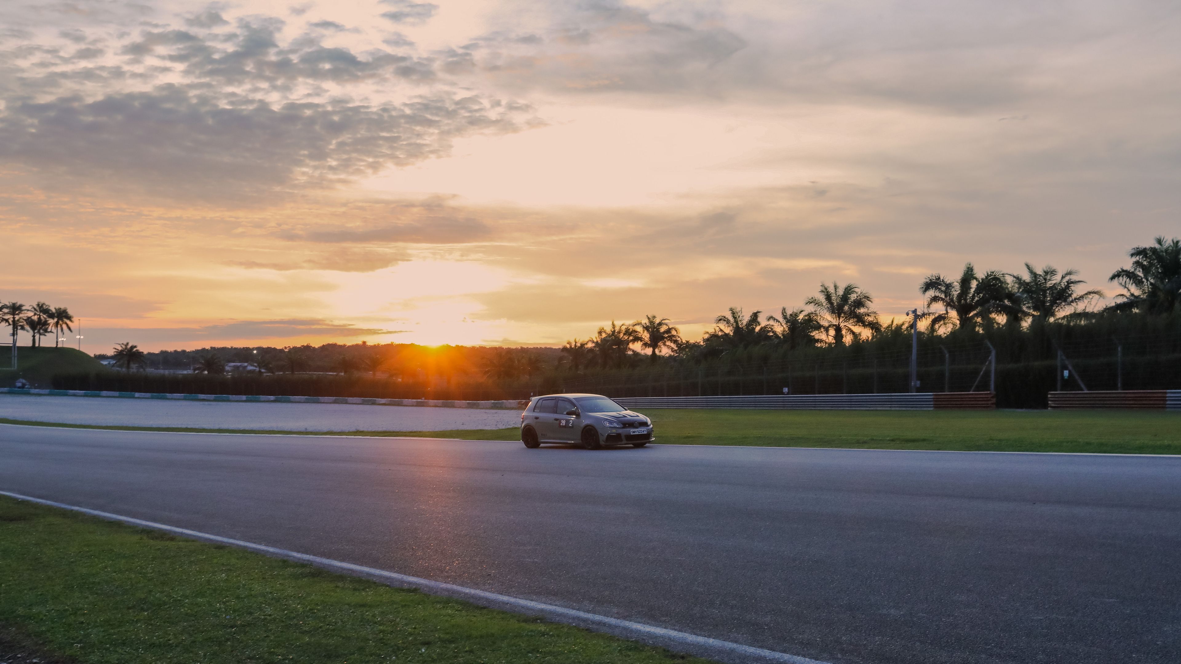 Track hot laps A car drives on a racetrack at sunset, with palm trees and a mostly clear sky in the background.